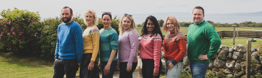 people standing facing camera wearing colourful knitwear jumprers from Harley of Scotland